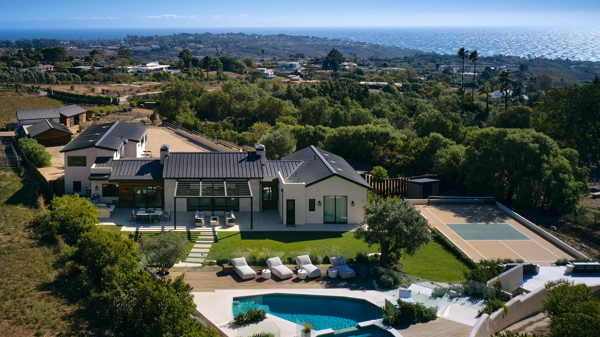 Aerial view of a Malibu hillside home in the Santa Monica Mountains, the slope running down toward the ocean behind it