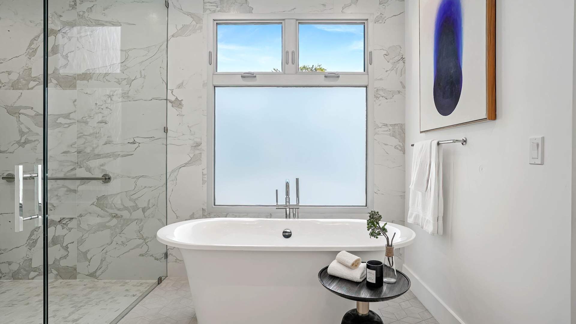 Stylish bathroom remodel with marble tile shower, freestanding tub, and contemporary art on white walls.