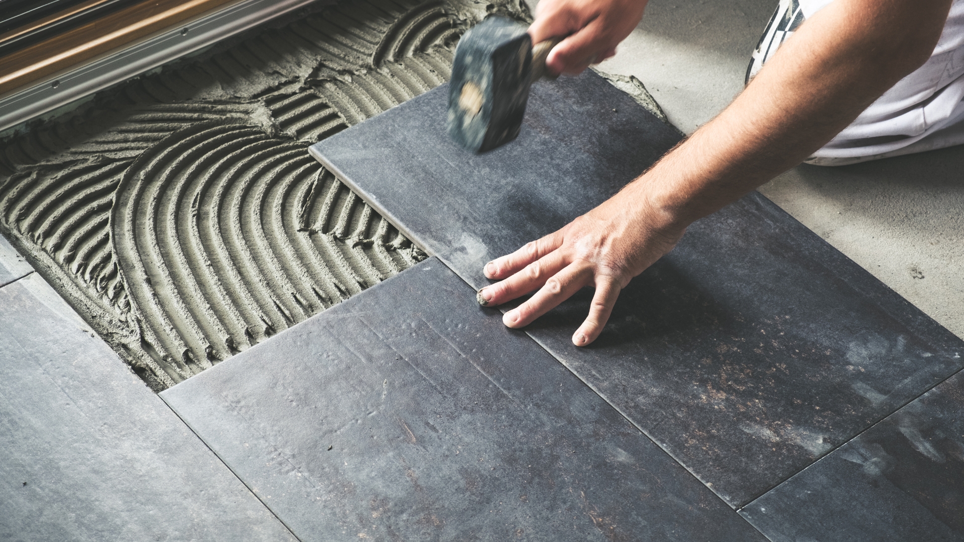 A tile contractor using a mallet to install the black tile on the floor