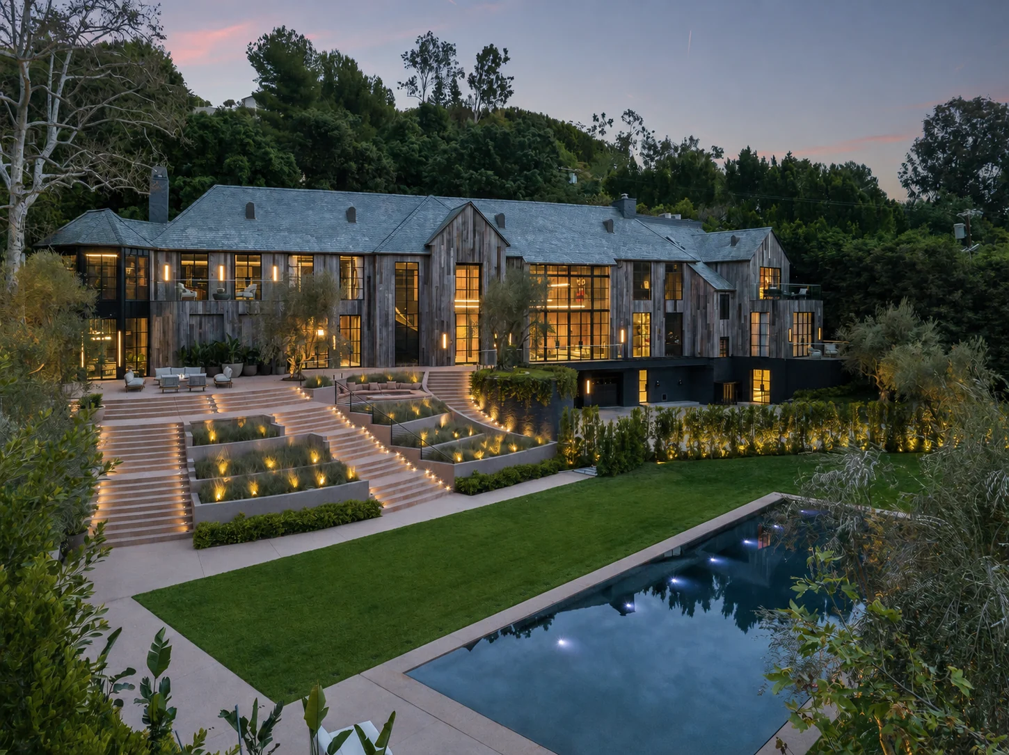 Benedict Canyon home at dusk, with illuminated windows, terraced gardens and a pool.