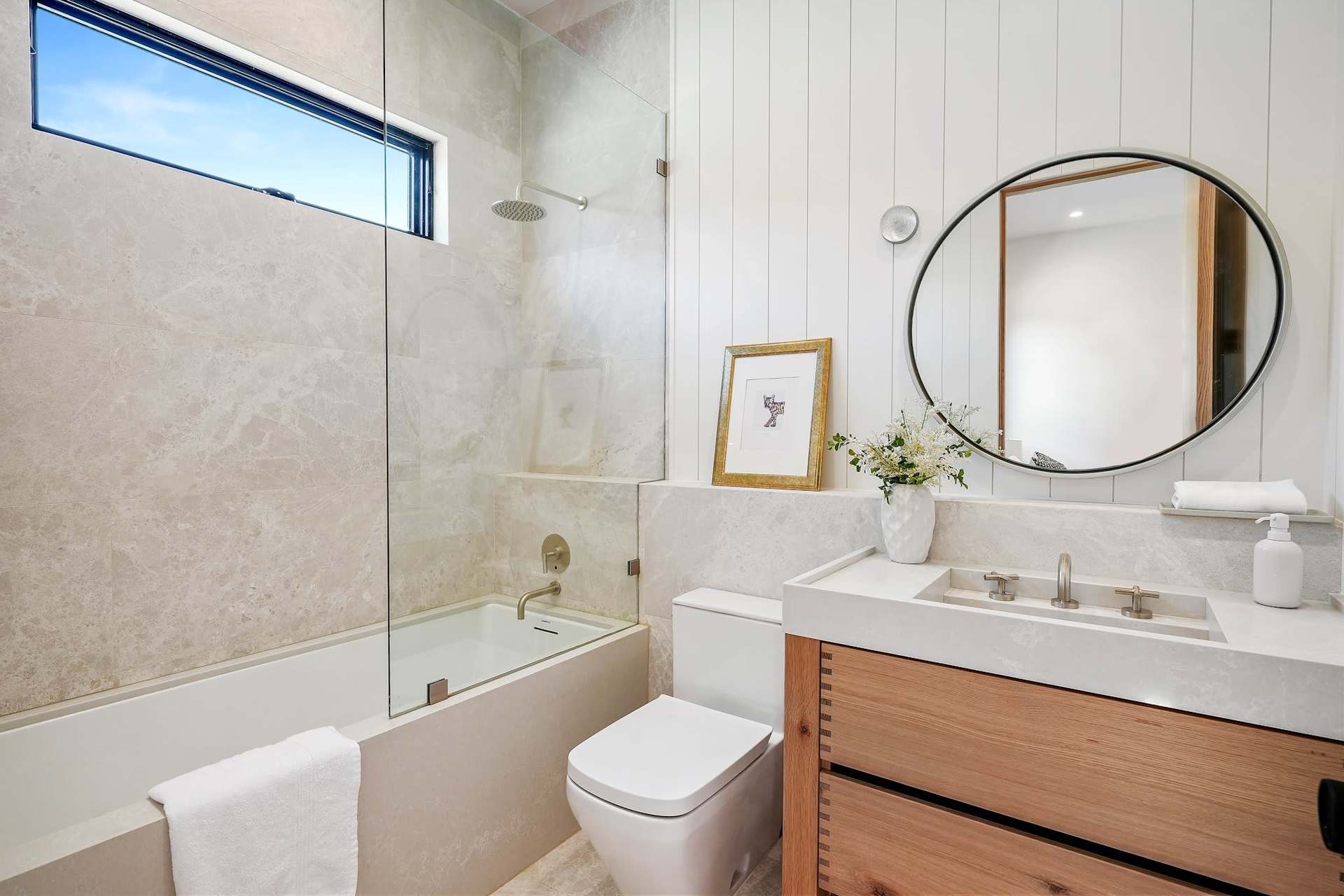 Contemporary bathroom with tub shower combo, stone tile walls, round mirror, and wood vanity