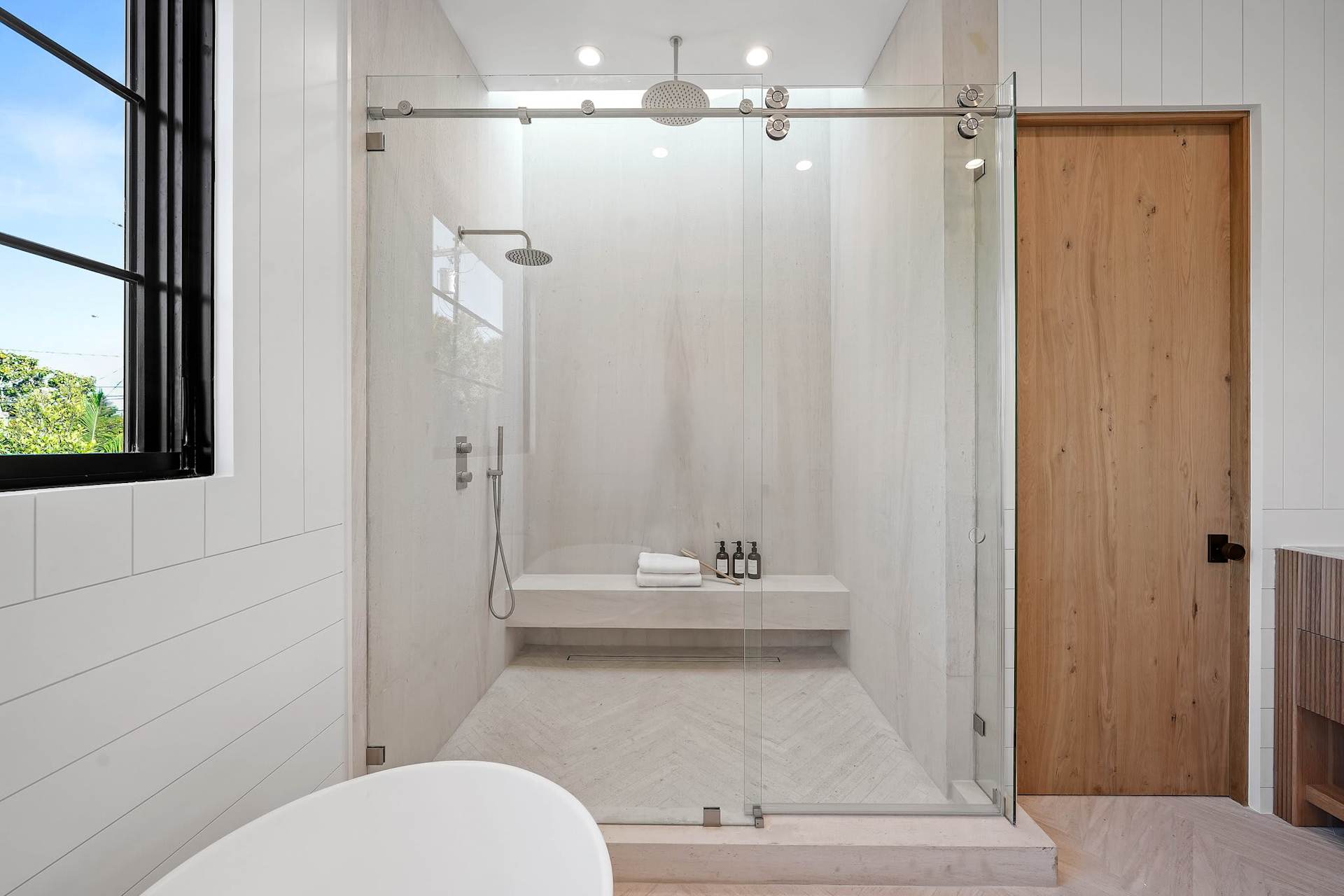 Spa-style primary bathroom with glass walk-in shower, bench seating, and minimalist modern design