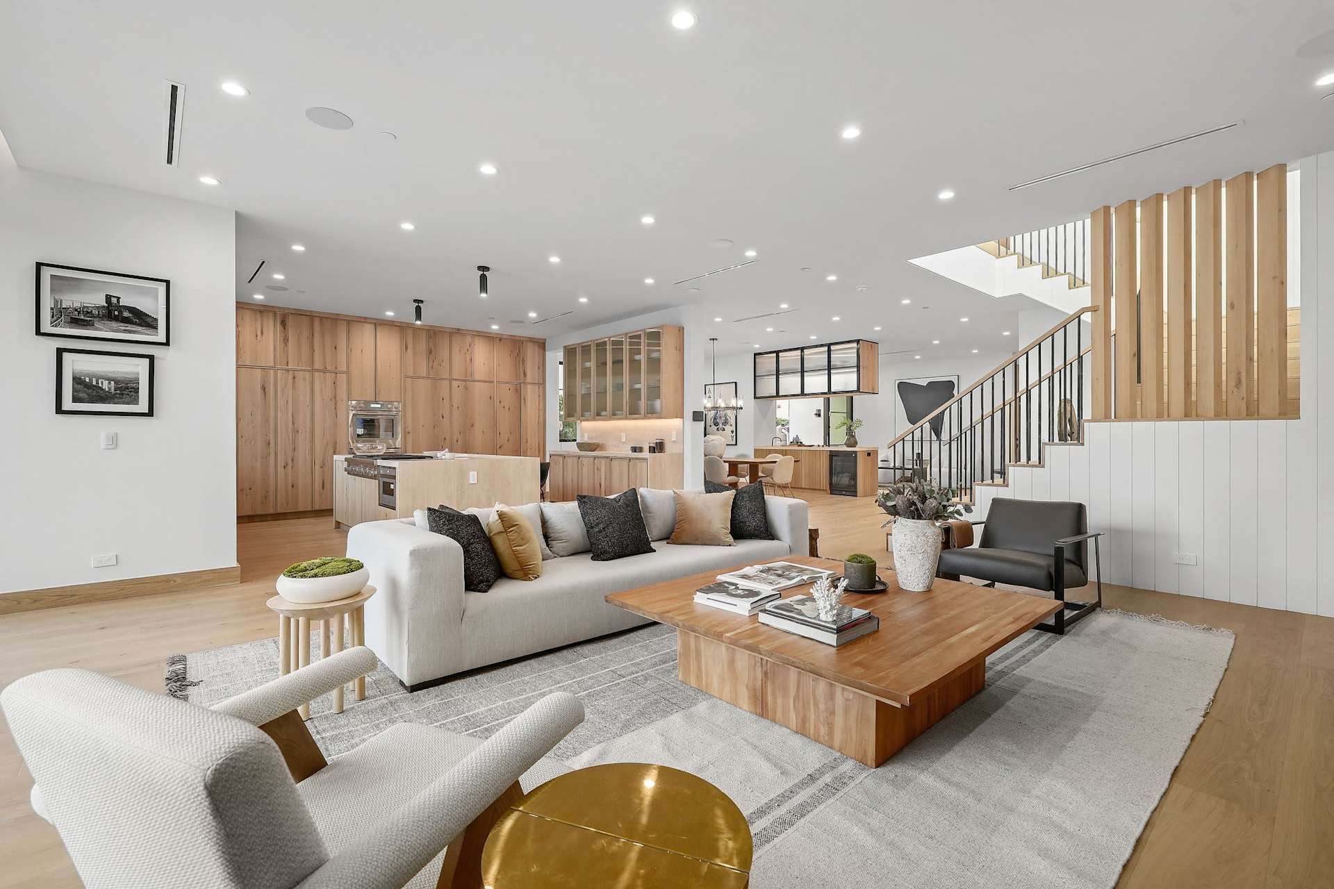 Bright open-concept living room with modern seating area, wood flooring, recessed lighting, and custom kitchen cabinetry