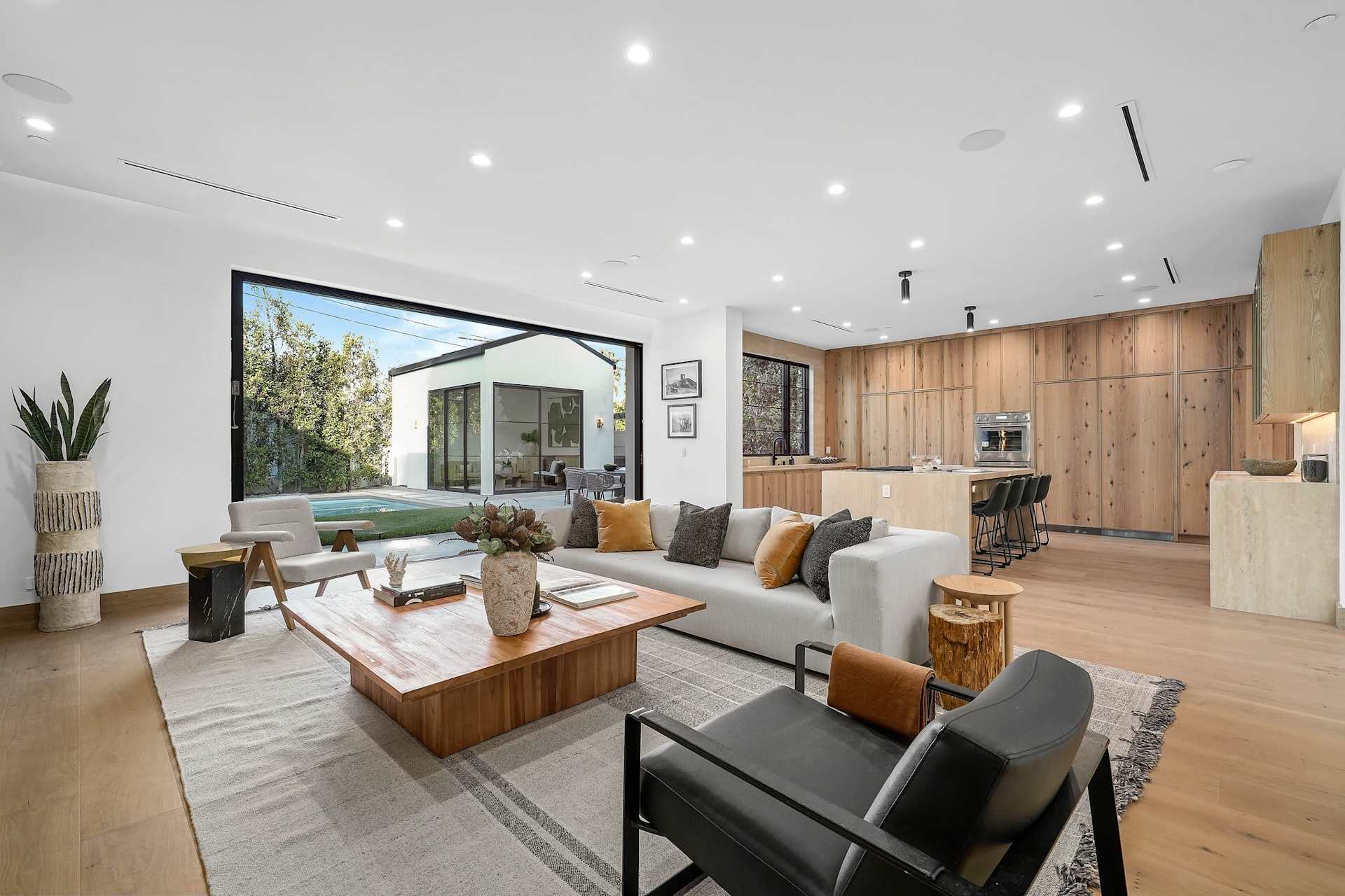 Spacious open living room connected to modern kitchen with large sliding glass doors and natural wood finishes