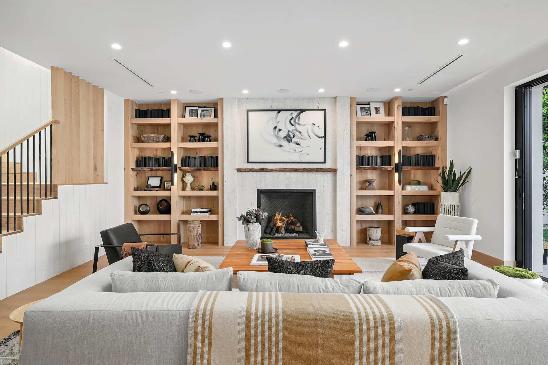 Elegant living room with built-in wood shelving, modern fireplace, designer seating, and warm natural finishes