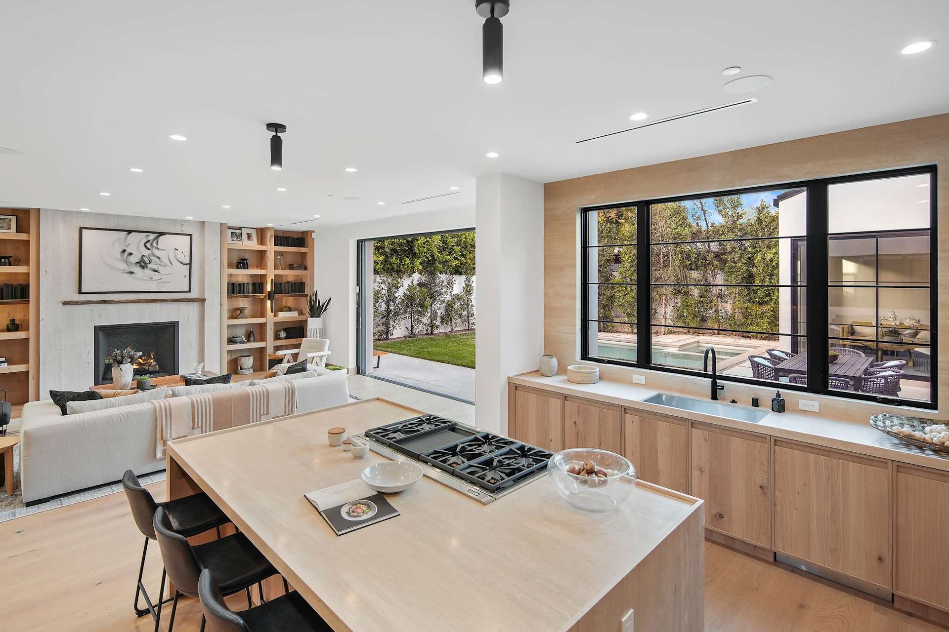 Luxury kitchen with large island, open living area, wide backyard access, and pool view through glass doors