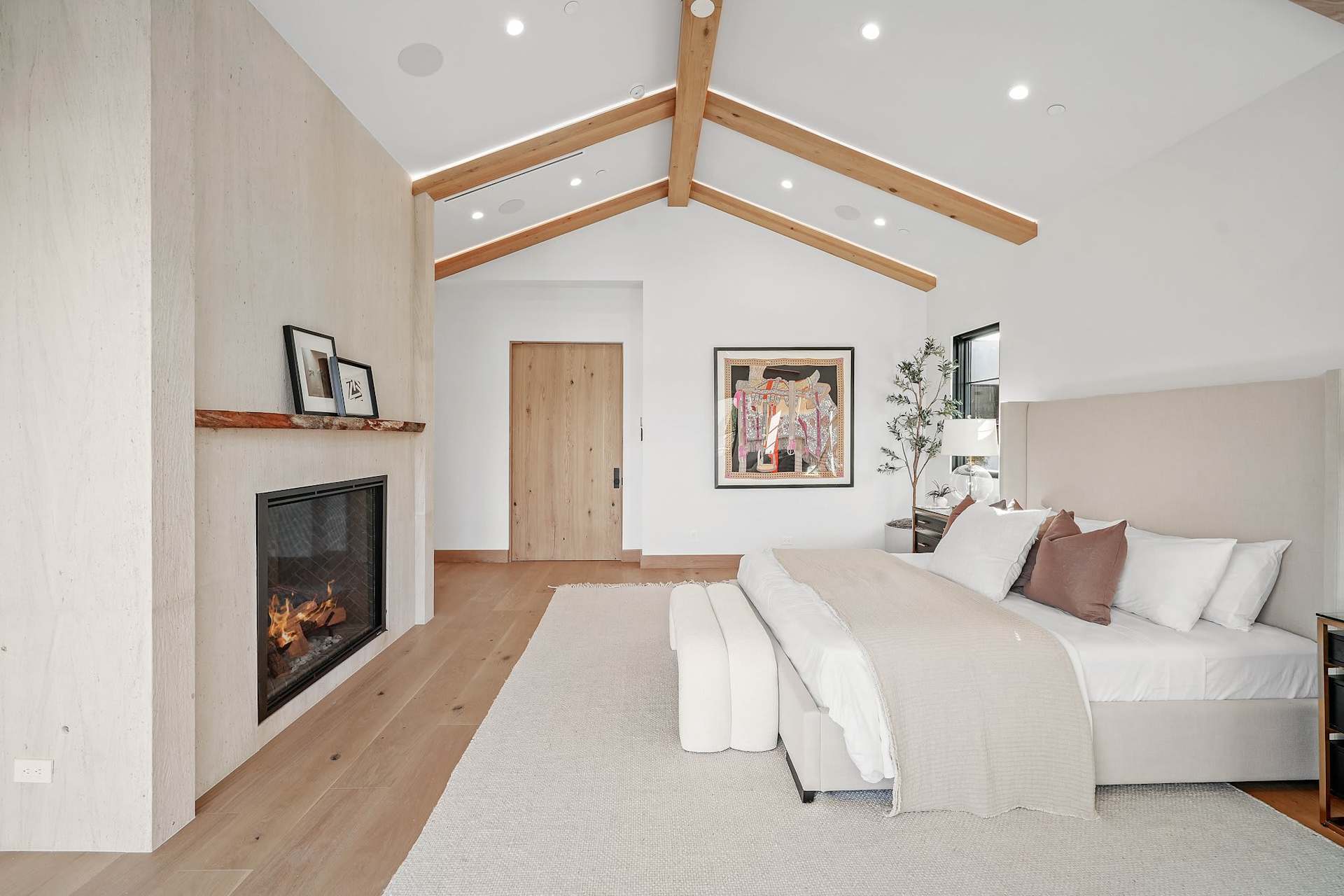 Spacious primary bedroom with vaulted ceiling, exposed beams, fireplace, and soft neutral design