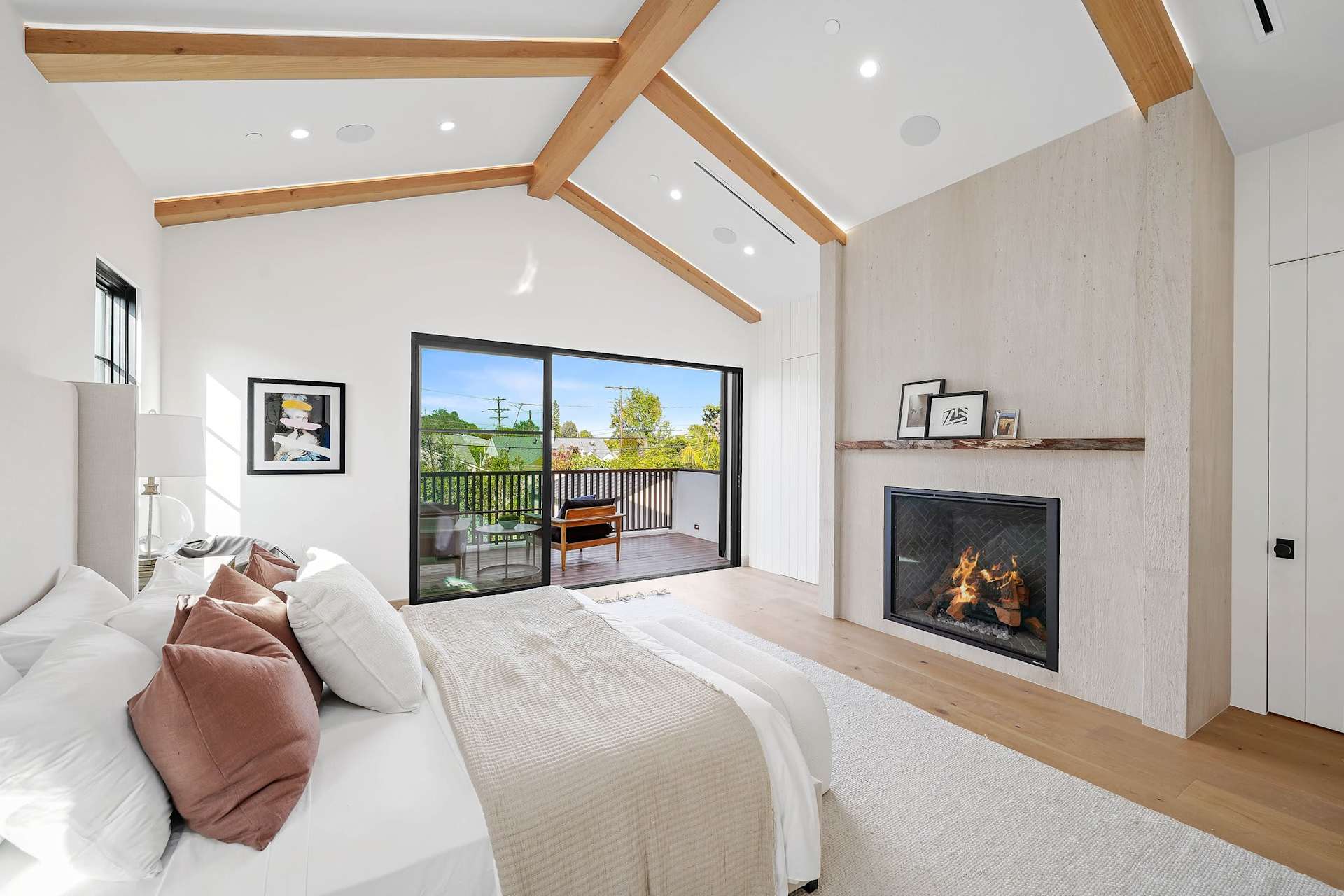 Luxury primary bedroom with private balcony access, fireplace, vaulted ceiling, and natural light
