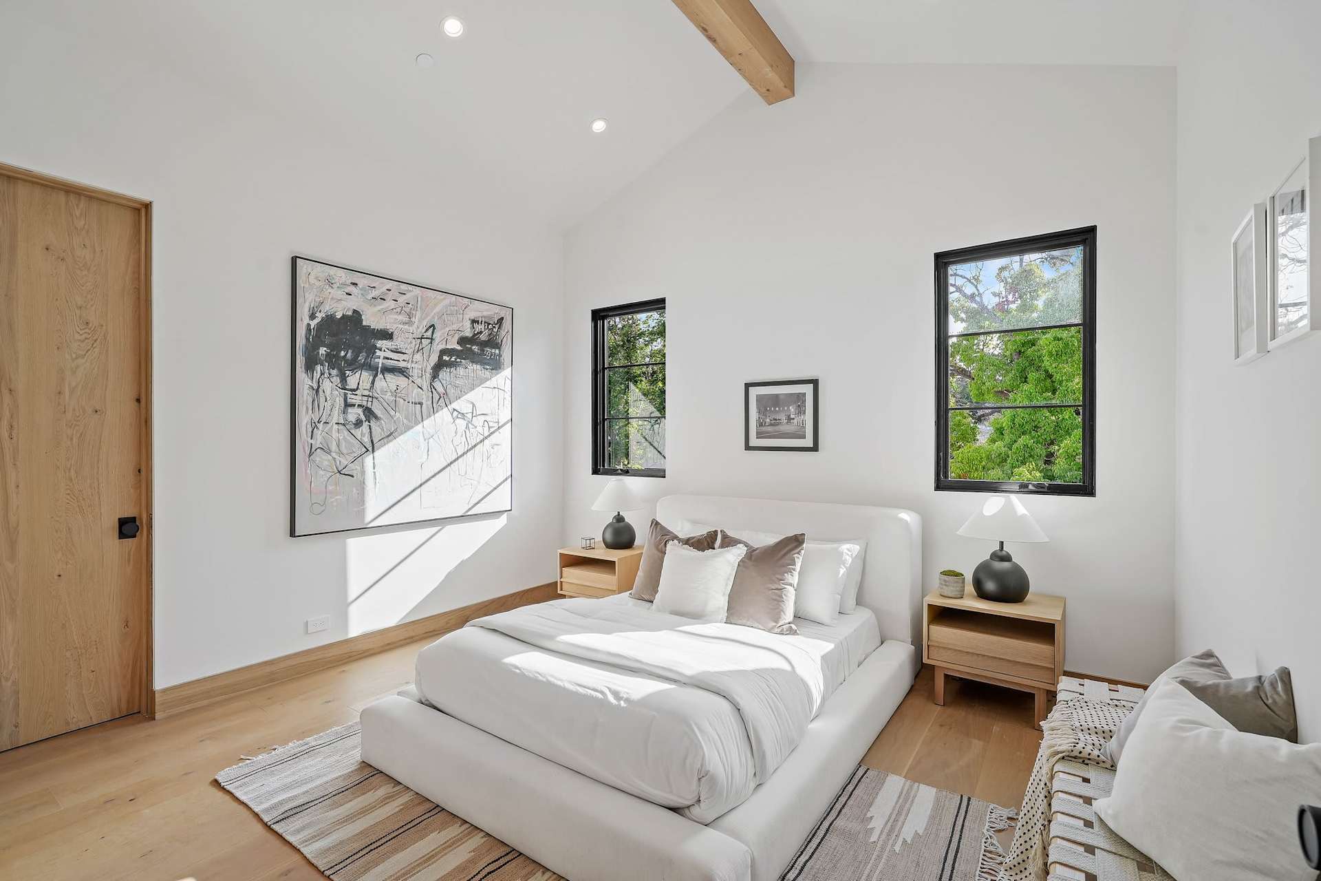 Bright modern bedroom with vaulted ceiling, neutral decor, wood flooring, and large windows