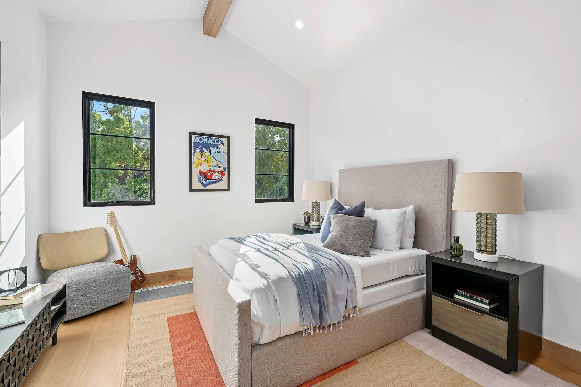 Stylish secondary bedroom with upholstered bed, natural light, modern furnishings, and clean finishes