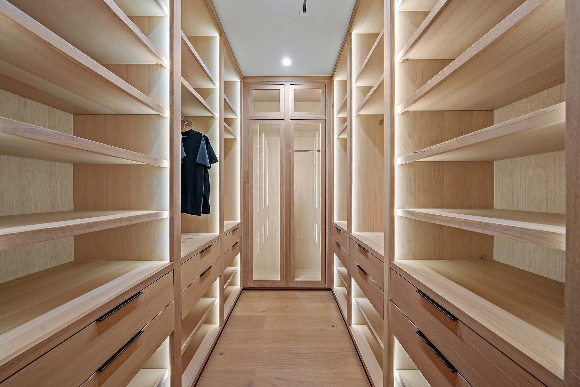 Elegant primary bathroom with double vanity, wood cabinetry, tall mirrors, and modern finishesLuxury custom walk-in closet with built-in shelving, drawers, lighting, and wood finishes