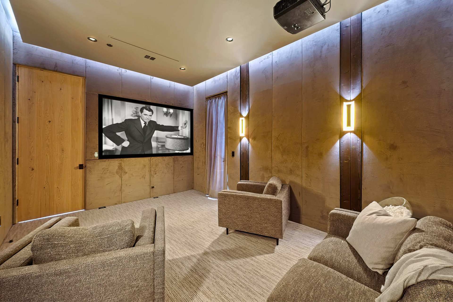 Private home theater room with projector screen, lounge seating, acoustic wall panels, and ambient lighting
