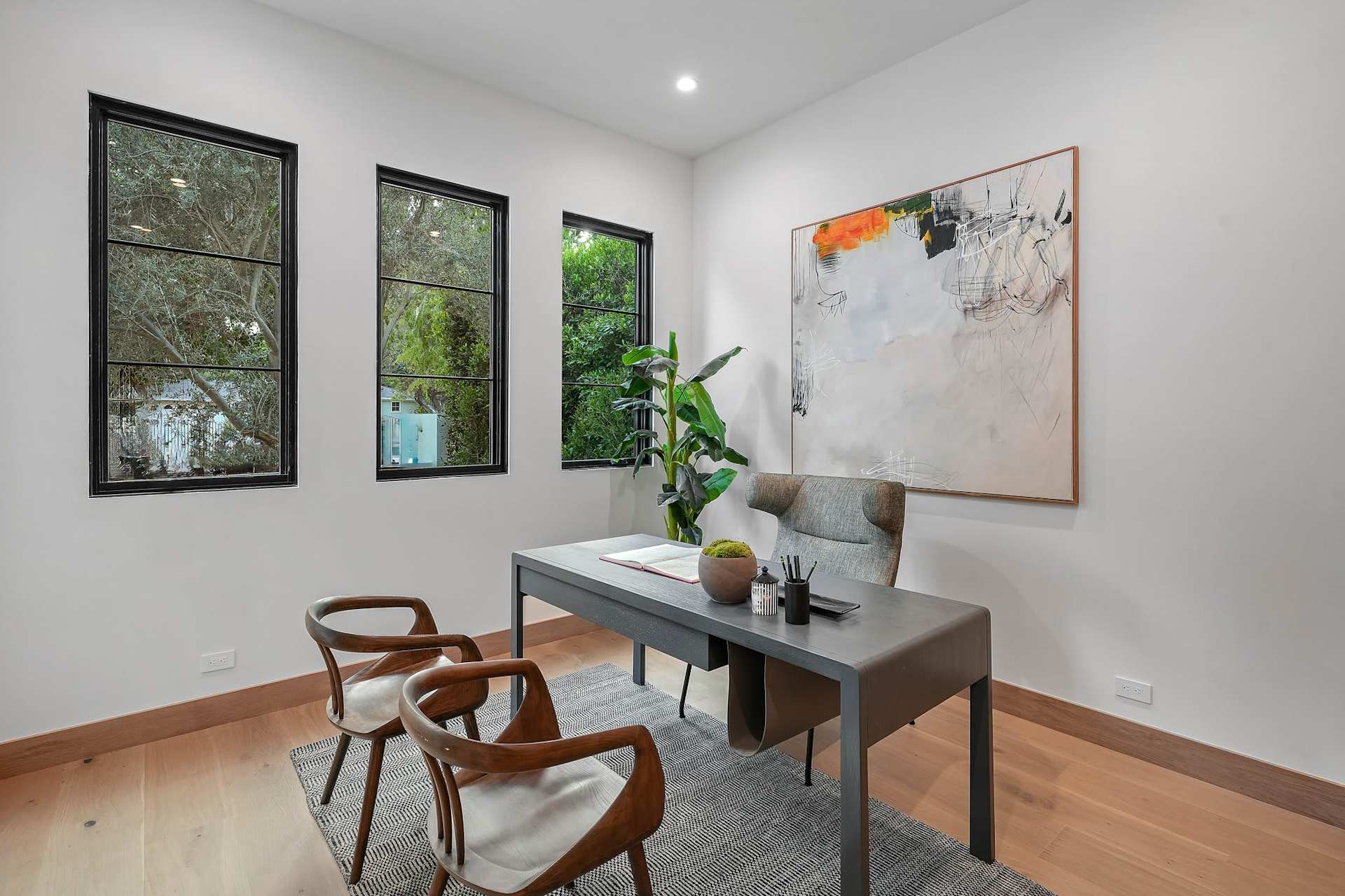 Modern home office with executive desk, guest chairs, large artwork, and natural light from tall windows