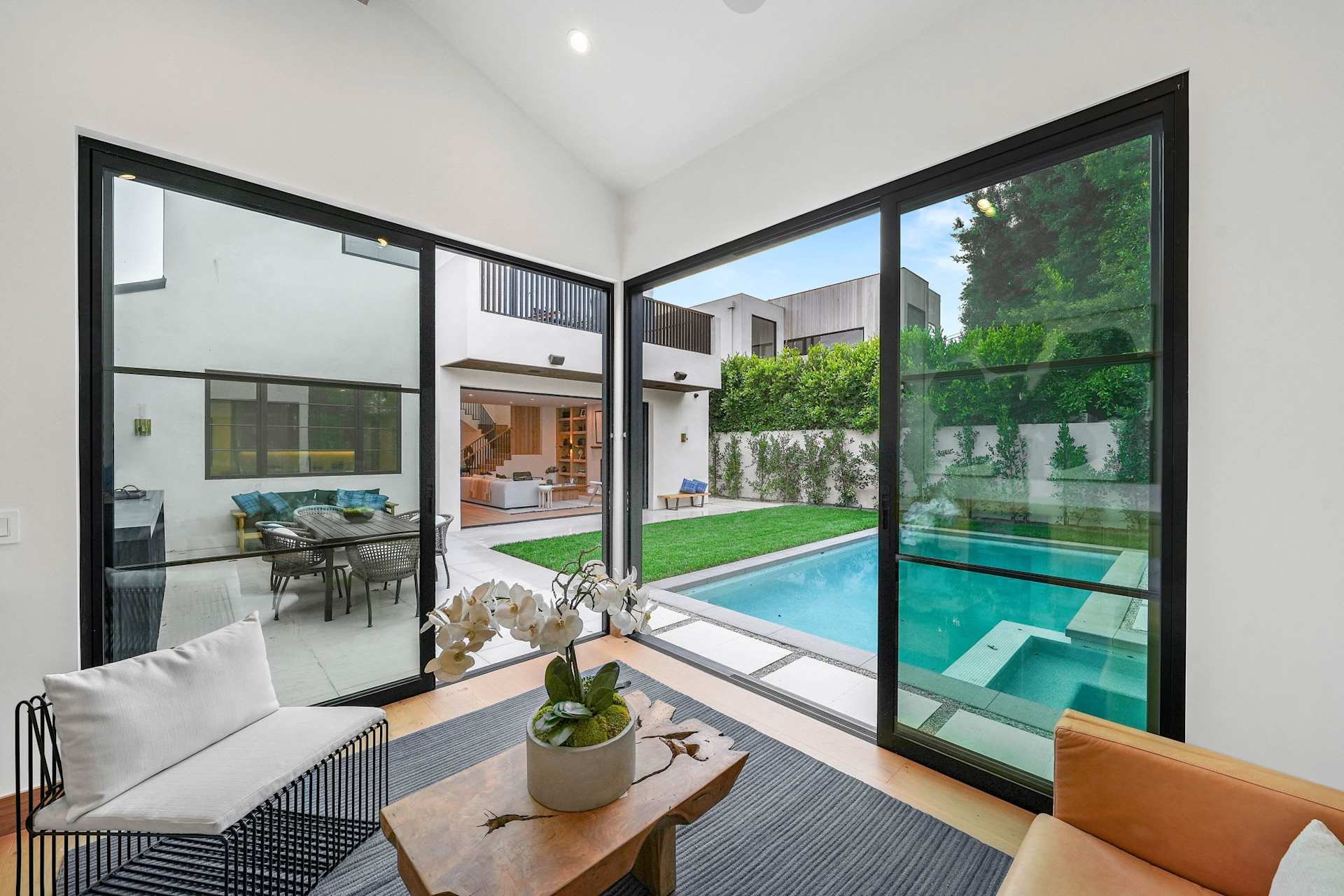 Modern poolside lounge inside guest house with floor-to-ceiling glass doors and backyard pool views