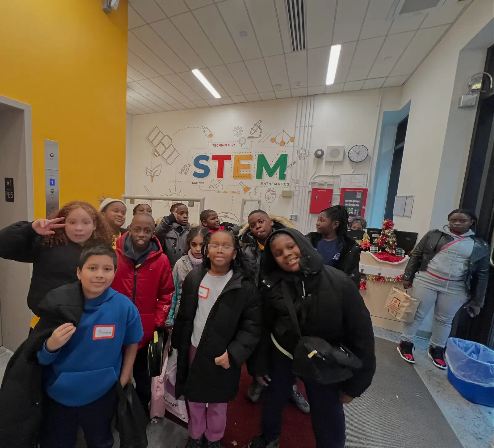 Students posing in STEM classroom with colorful wall display