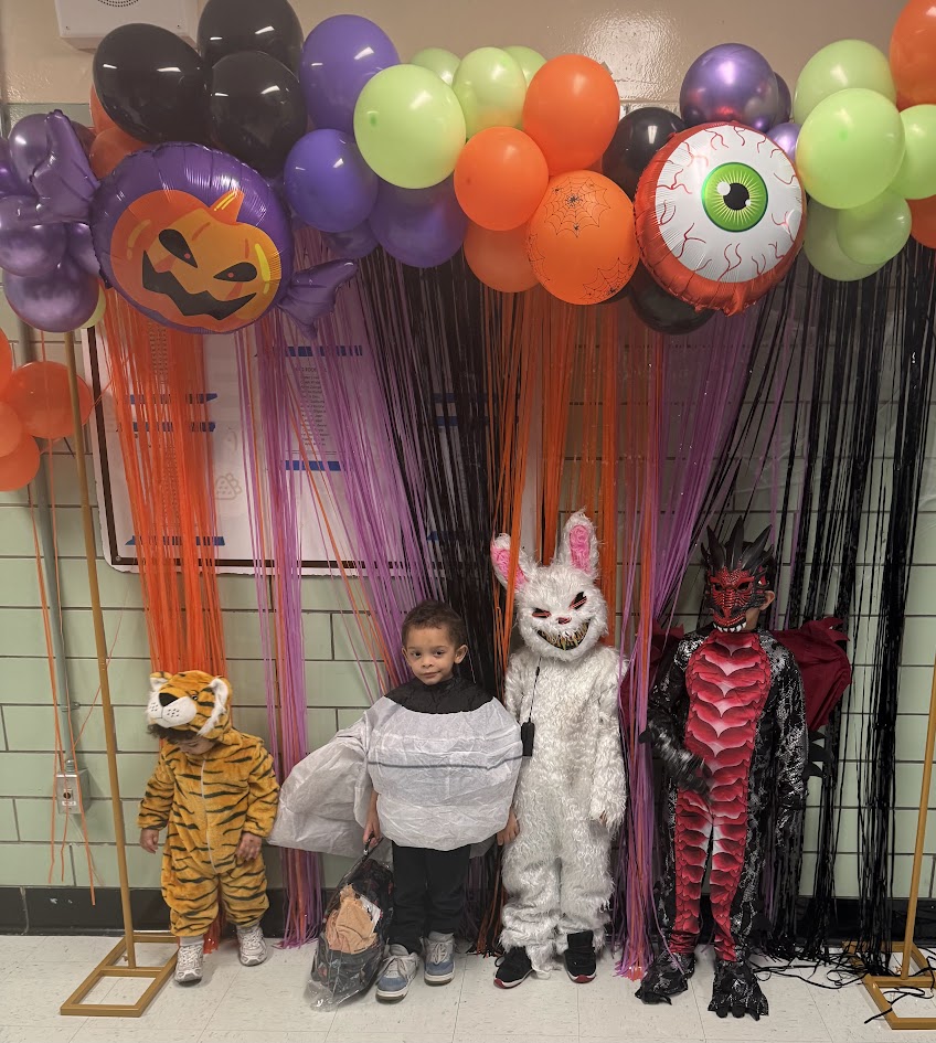 Students in Halloween costumes posing under festive balloon arch