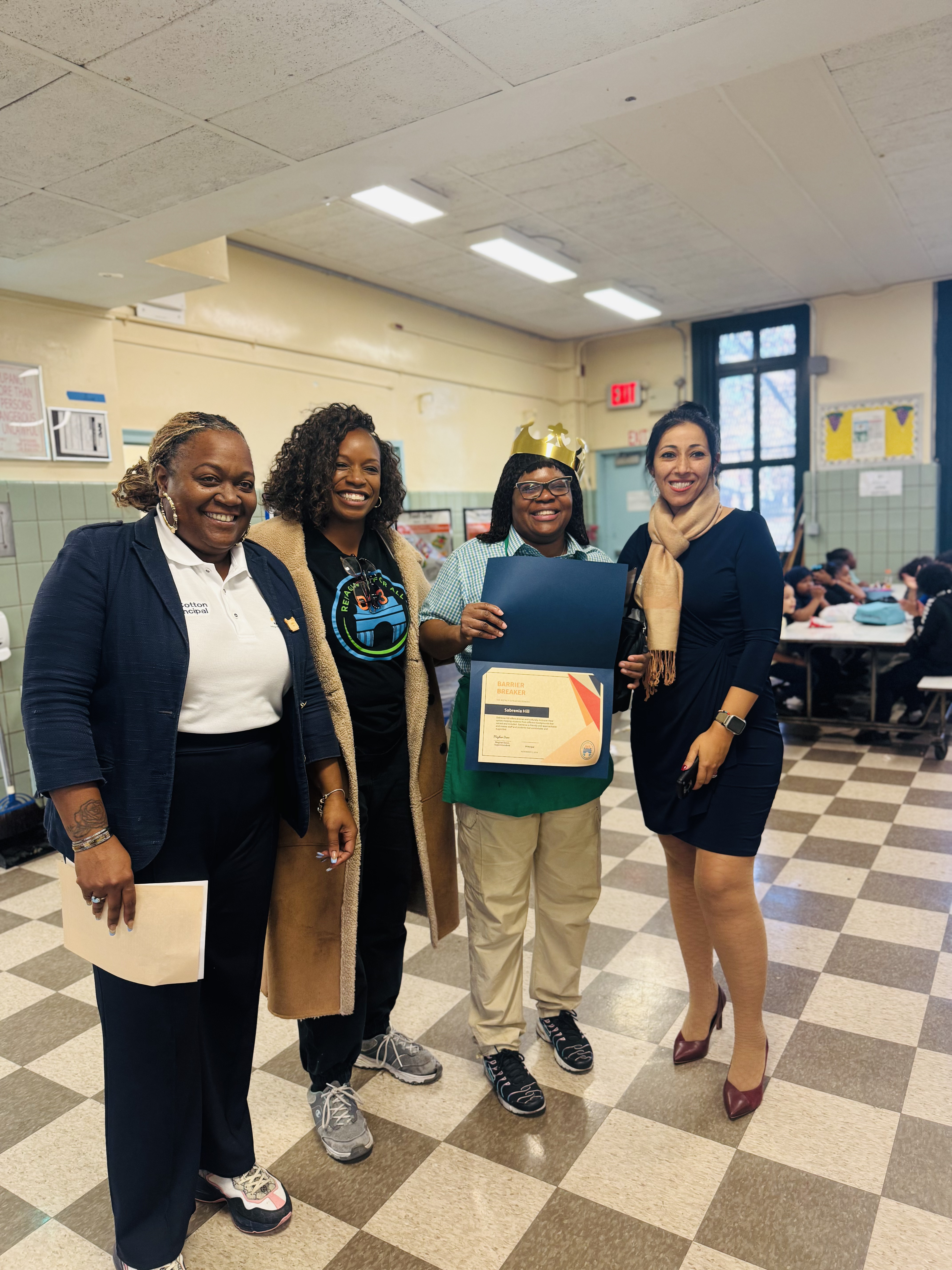Student wearing crown receives award certificate from school staff members