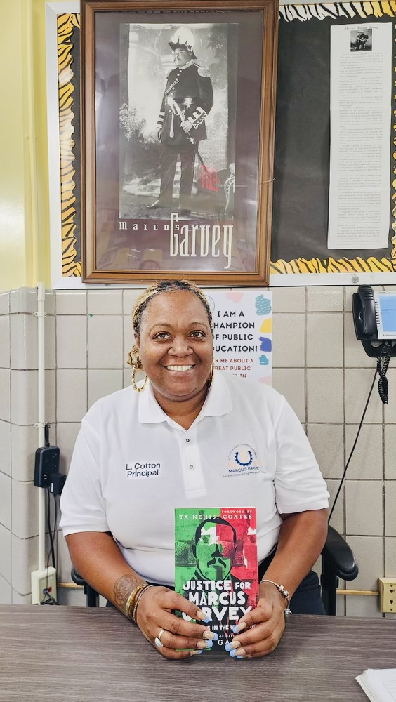 Principal L. Cotton holding Justice for Marcus Garvey book at school