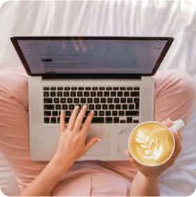 Person typing on a laptop while holding a cup of latte with leaf latte art.