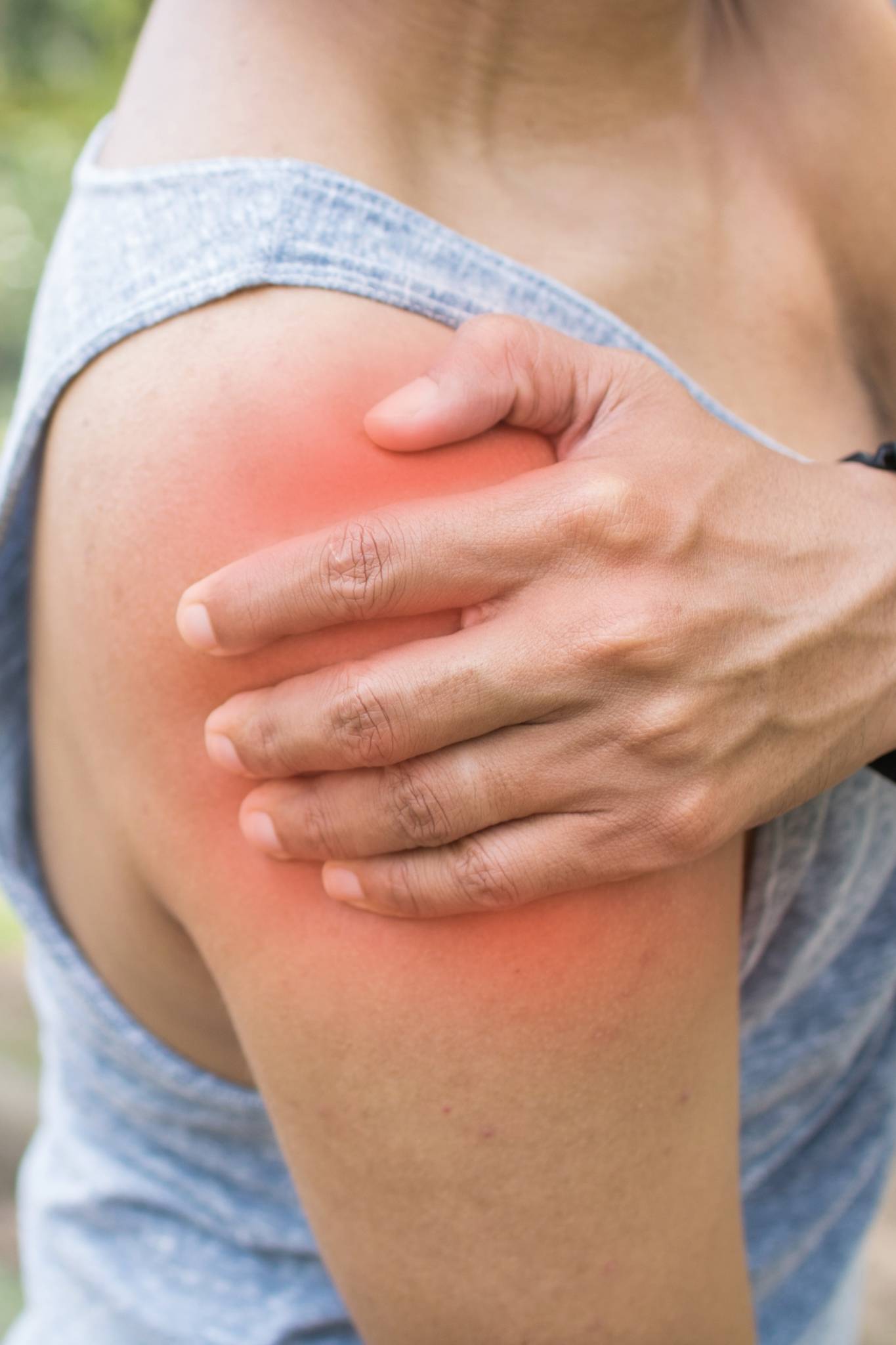 Close-up of a person clutching their shoulder with a red highlighted area indicating pain or inflammation.