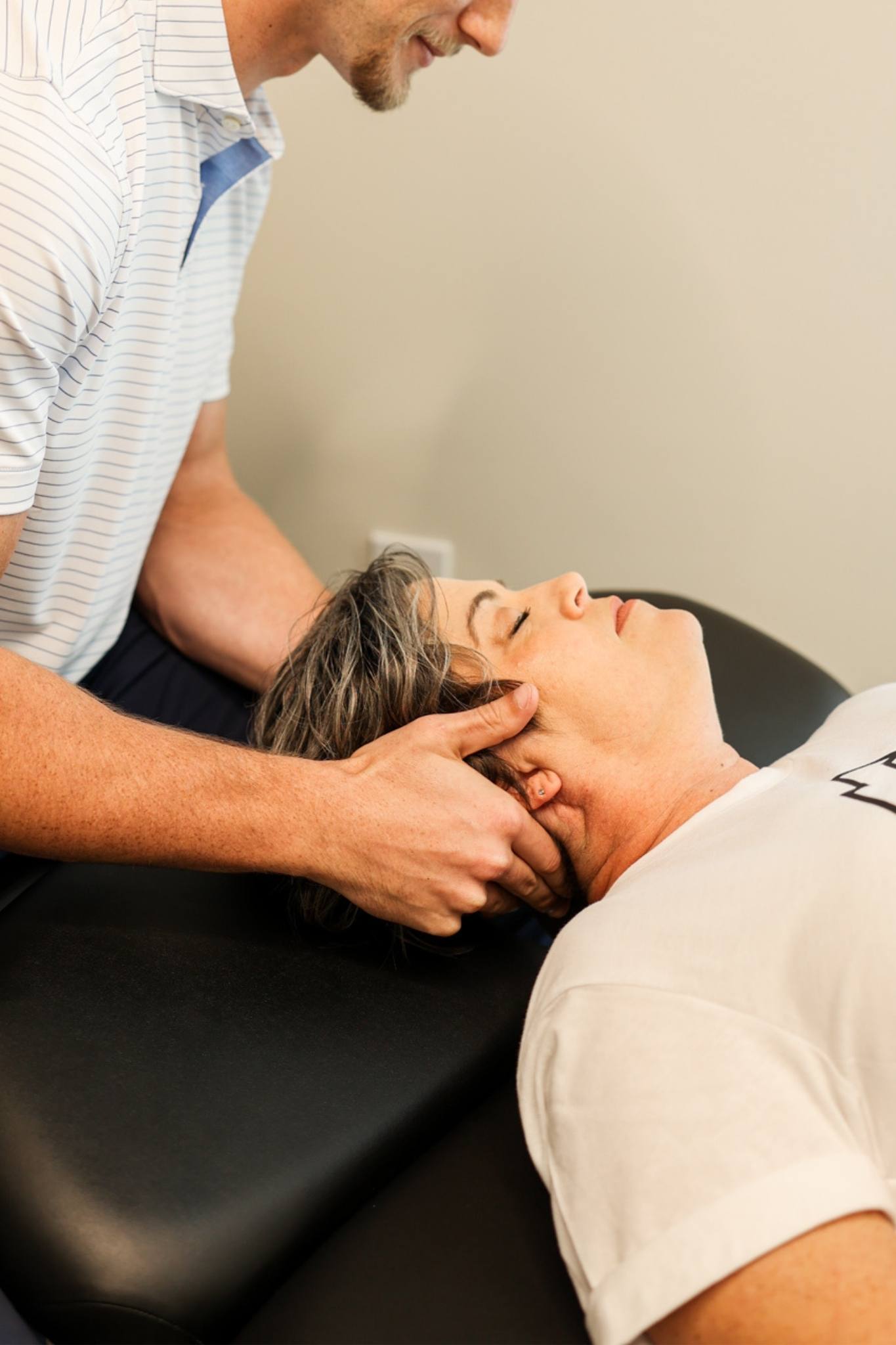Healthcare practitioner, Dr. Matt Amos from Highland Spine + Sport supports a woman’s head and neck during a treatment session on a padded therapy table.