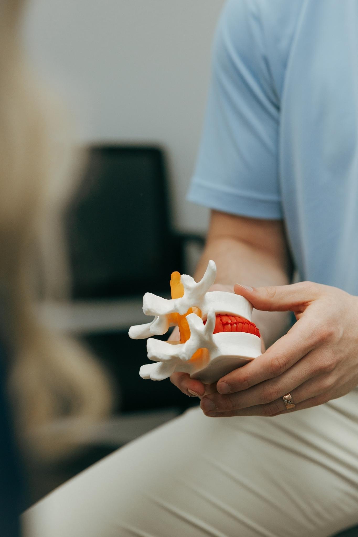 Healthcare practitioner, Dr. Matthew Amos from Highland Spine + Sport, holds a spine model showing a bulging disc and nerves while explaining spinal health to a patient.