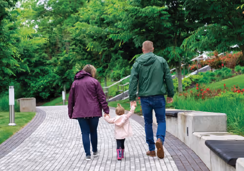 A toddler walking with their parents on The Trail