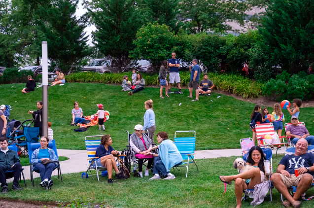 Many people sitting on lawn chairs in the grass at an event