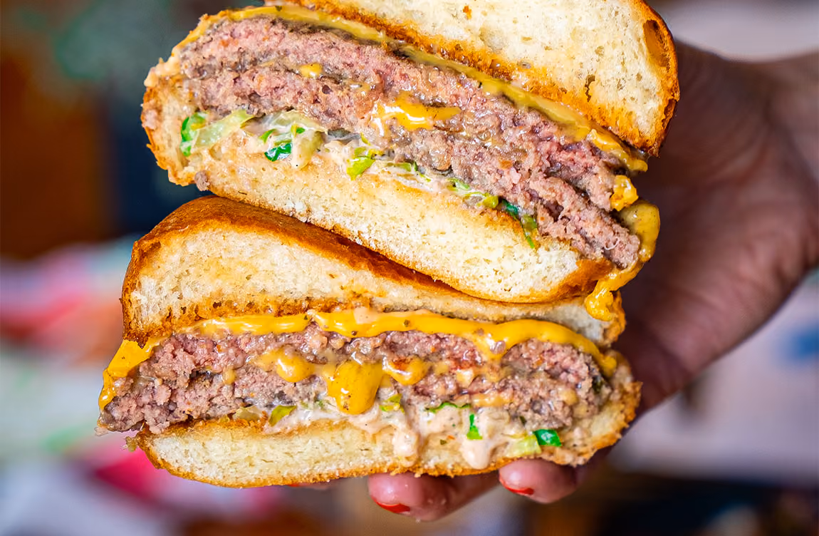 someone holding two halves of a cheeseburger in their palm