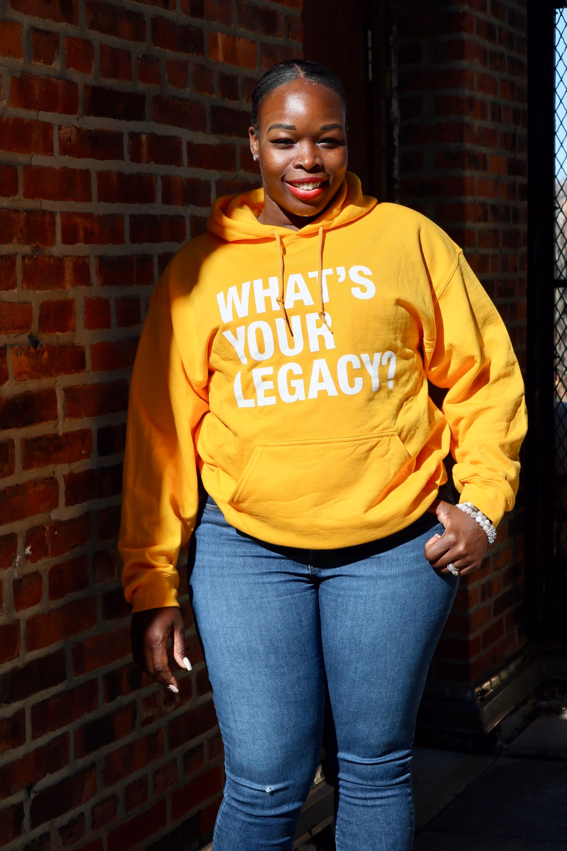 Woman smiling in yellow What's Your Legacy hoodie outside