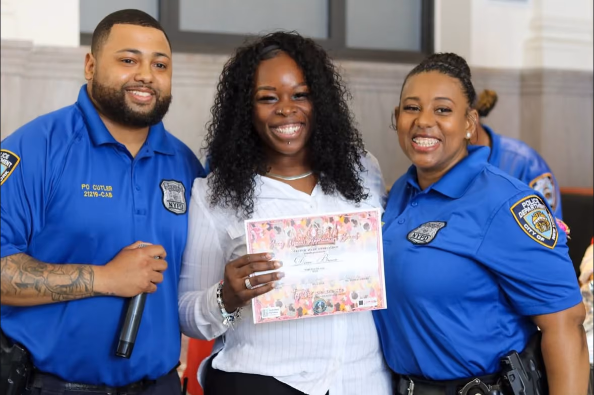 Student receiving certificate of appreciation from two NYPD officers