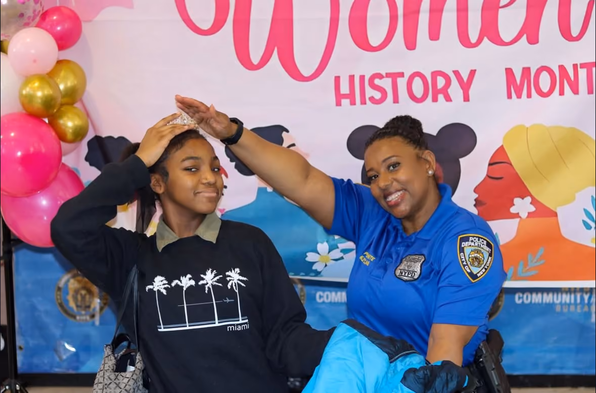NYPD officer placing a crown on a student at Women's History Month event
