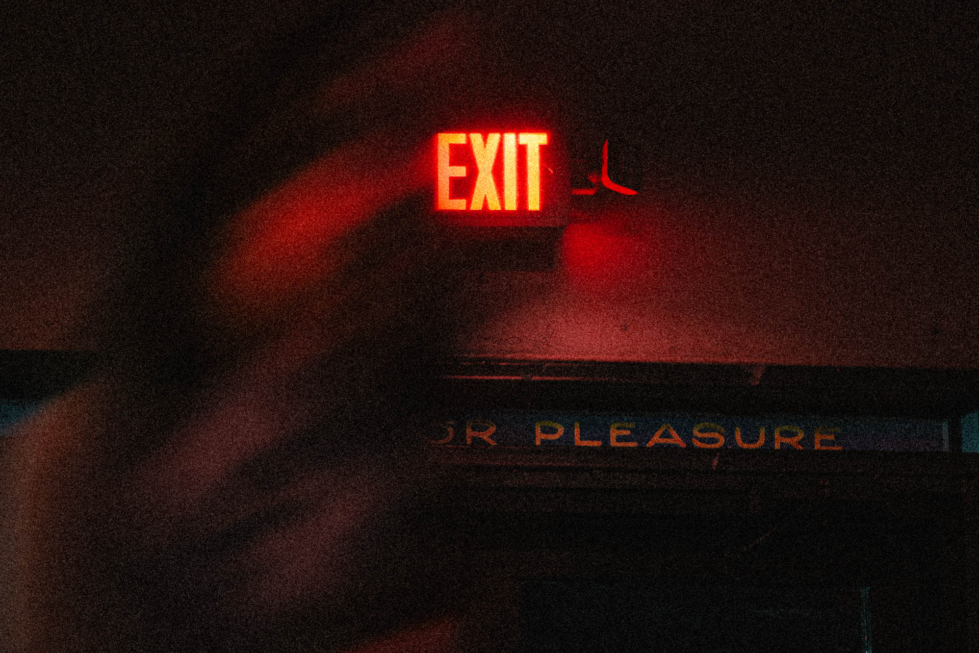 a neon exit sign with a woman walking under it