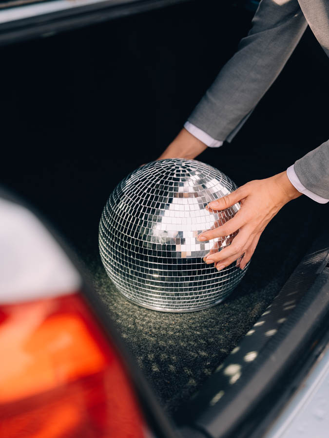 a person in a suit reaching for their disco ball head in the trunk