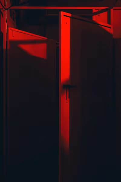 a slightly open bathroom stall in a red lit bathroom at night