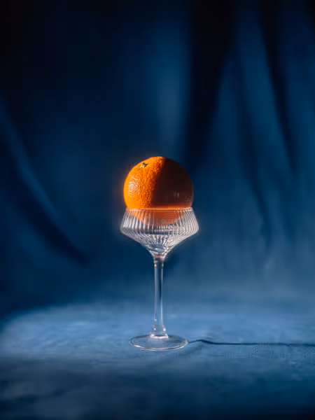 An orange inside a drinking glass on blue velvet