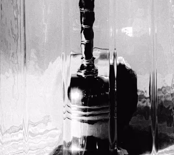 A close-up of an orange behind a small hand bell in a glass dome on velvet