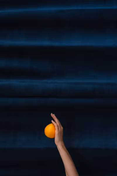 The hand of Saint Citrus holding an orange upwards in front of blue velvet