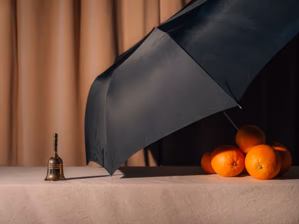 Oranges covered by an umbrella in front of a small bell