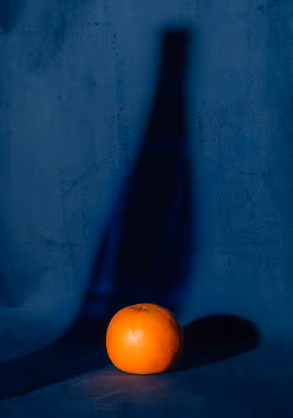 An orange with the shadow of a bottle on blue velvet