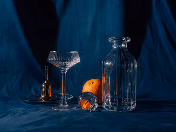 An orange behind different shaped glasses on blue velvet
