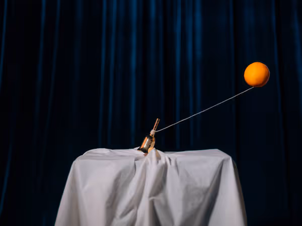A small golden hand bell being pulled by a floating orange on a string