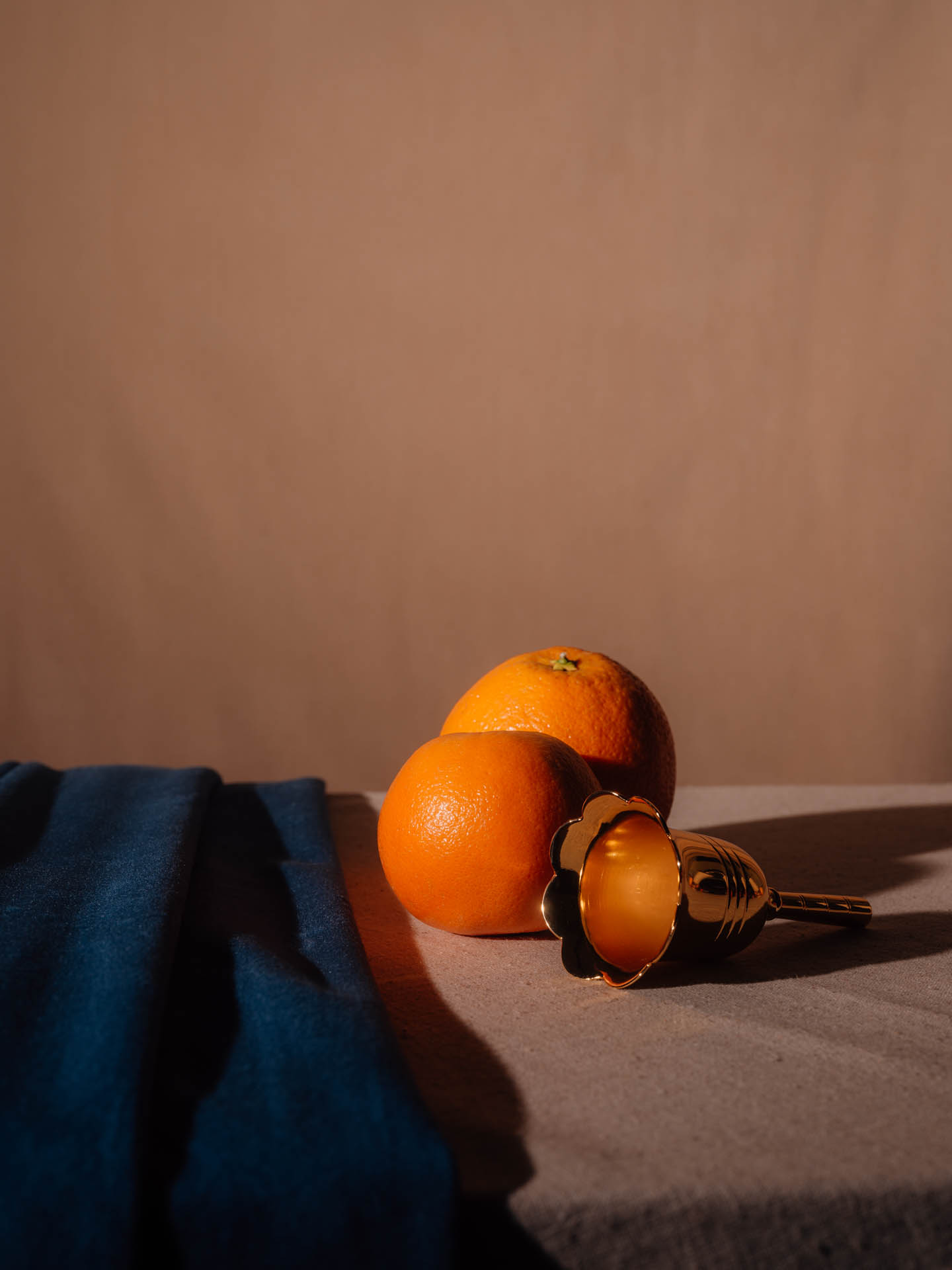 Two oranges with a small bell tilted over and blue velvet