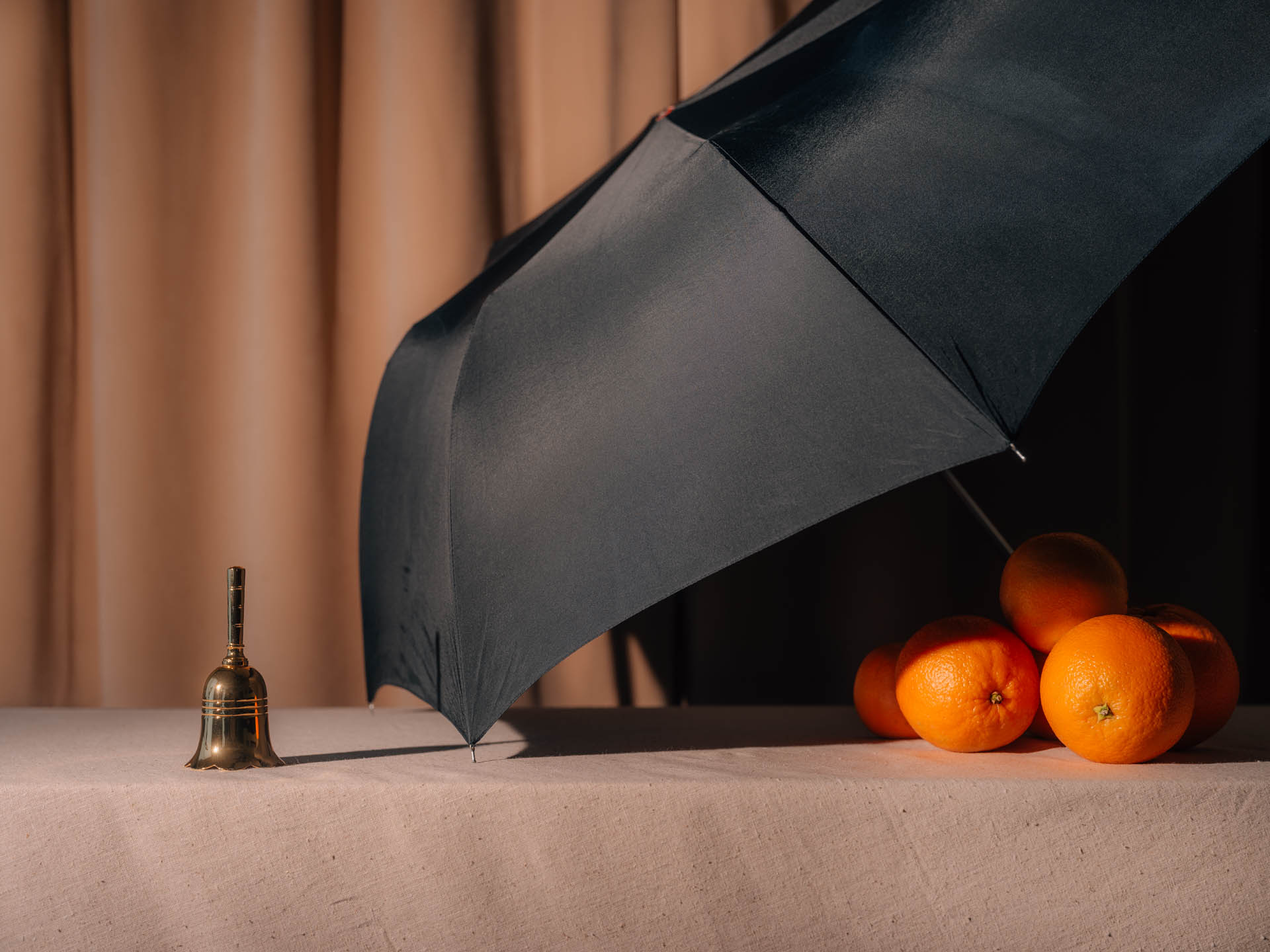 Oranges covered by an umbrella in front of a small bell