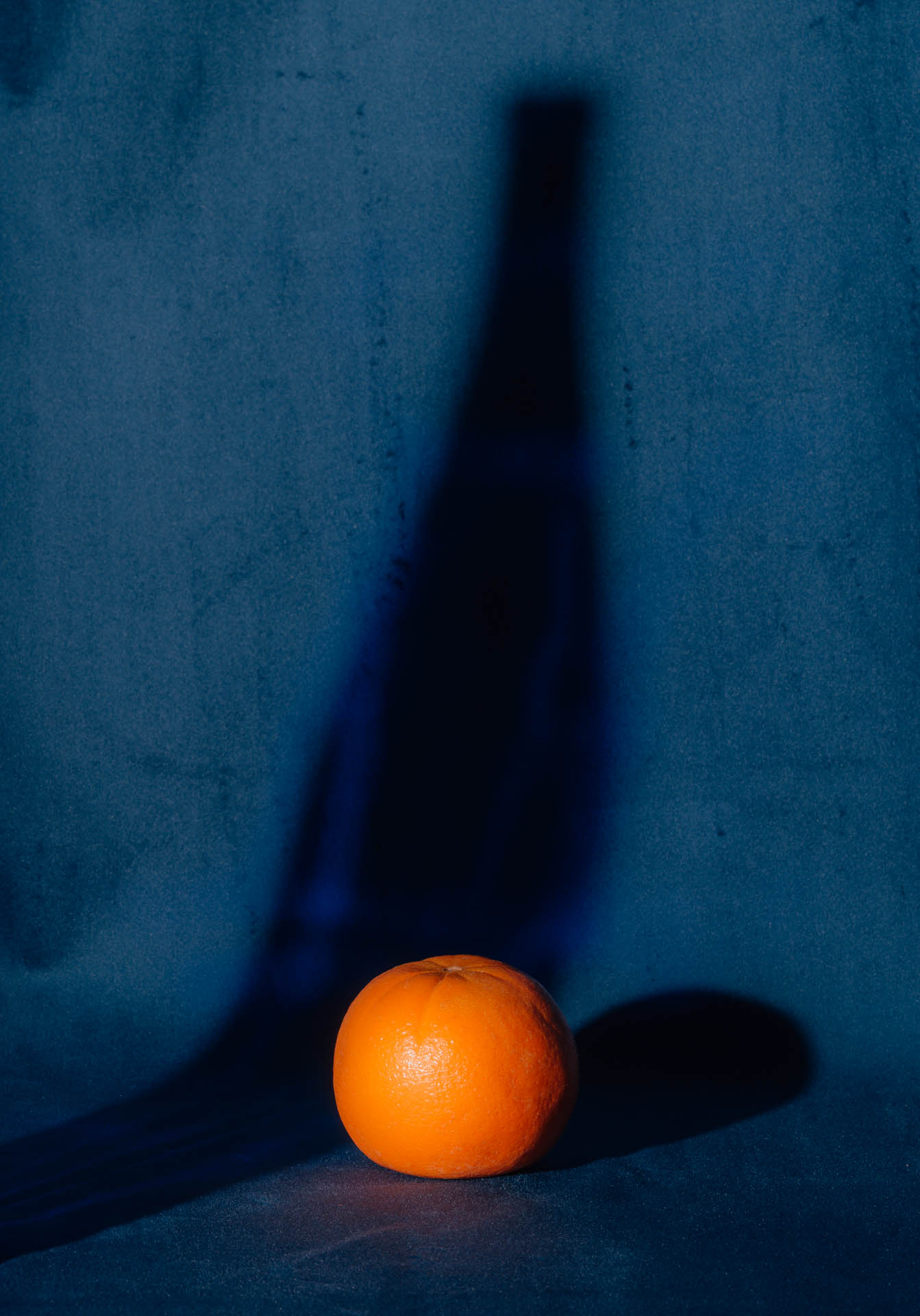 An orange with the shadow of a bottle on blue velvet