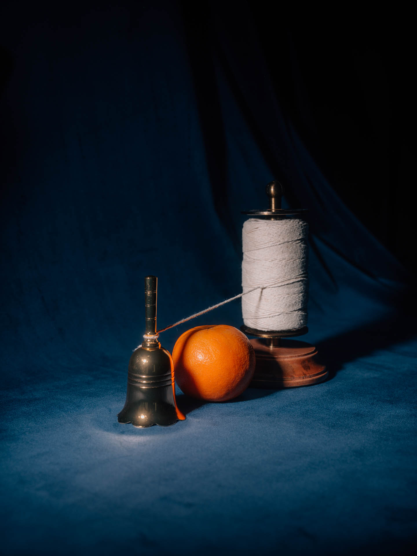An orange and a small bell with a spool of thread on blue velvet