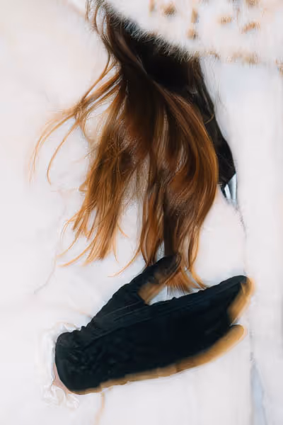 A woman's black glove with auburn hair in a white coat.