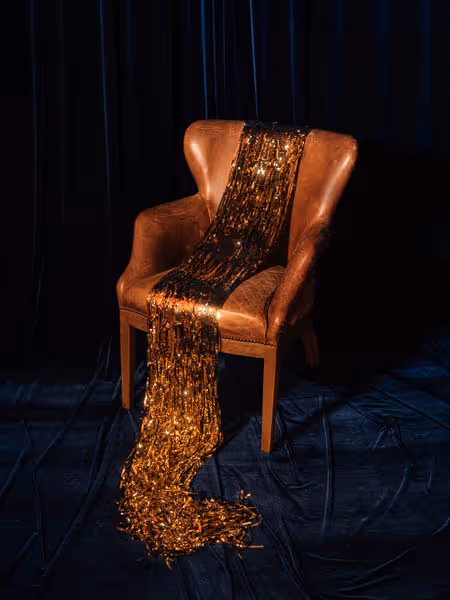 a brown leather chair with gold tinsel draped on it in the shape of a dress