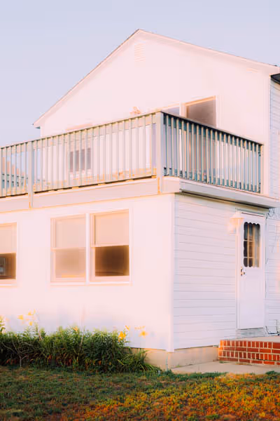 A glowing house in sunset with yellow flowers by the ocean
