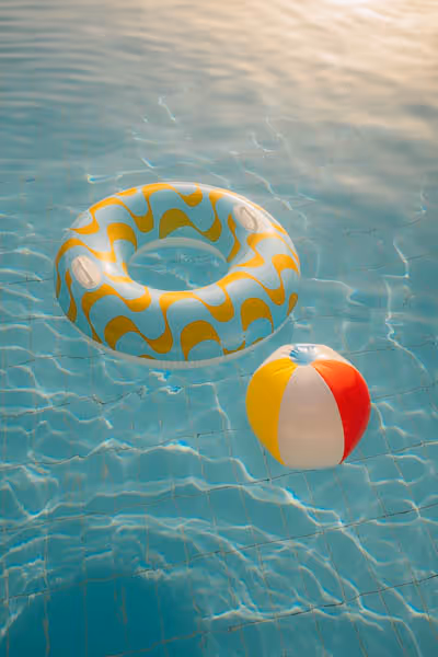 Beach ball and donut floating in a pool at sunset